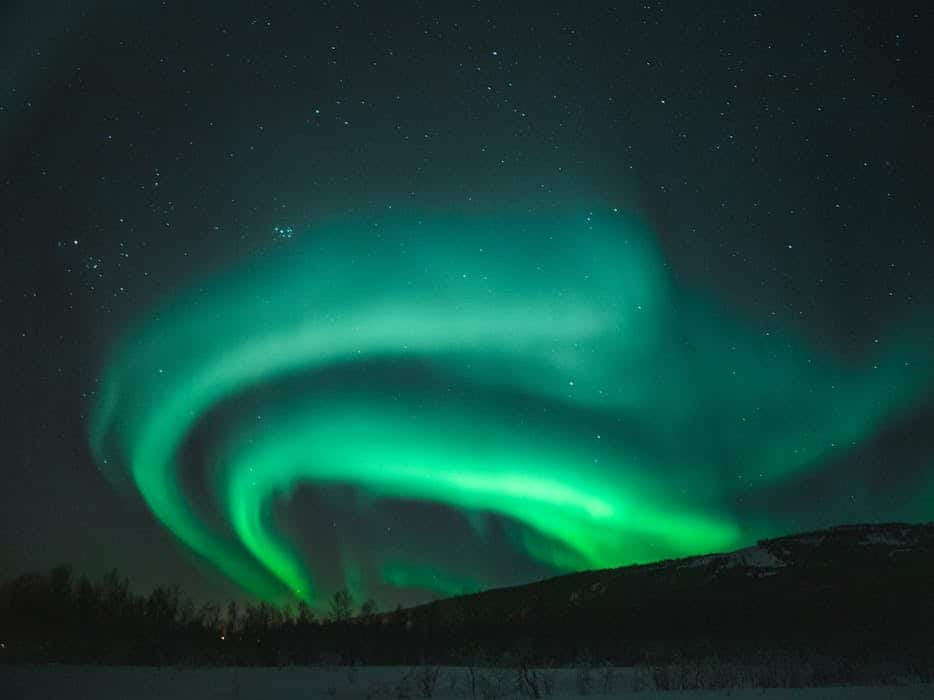 Spectacular view of the vibrant Northern Lights illuminating a snowy night sky in Norway.