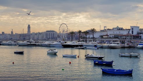 Coastal scene with boats docked at a harbor, featuring city skyline and Ferris wheel.