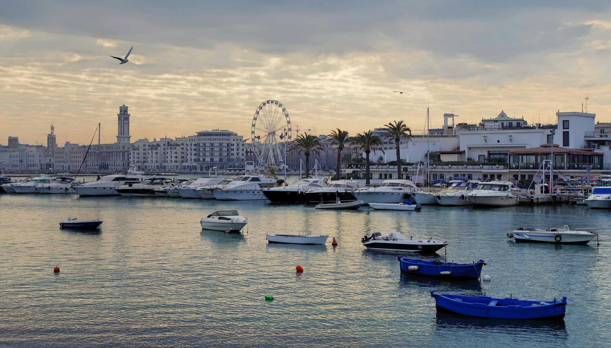 Coastal scene with boats docked at a harbor, featuring city skyline and Ferris wheel.