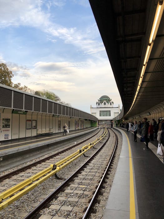 A view of a Vienna metro station under a bright sky with commuters waiting on the platform.